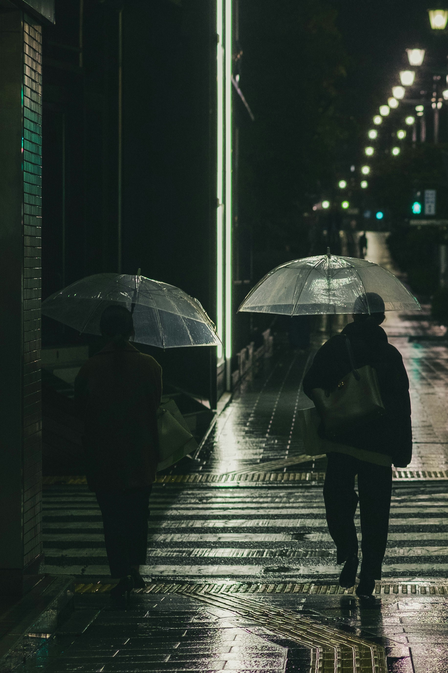 Silhouetten von Menschen mit Regenschirmen auf einer regennassen Straße