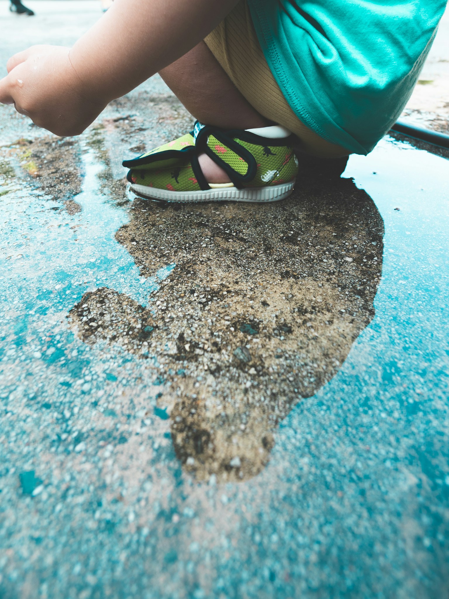 Anak bermain di genangan air mengenakan kaos hijau dan sandal