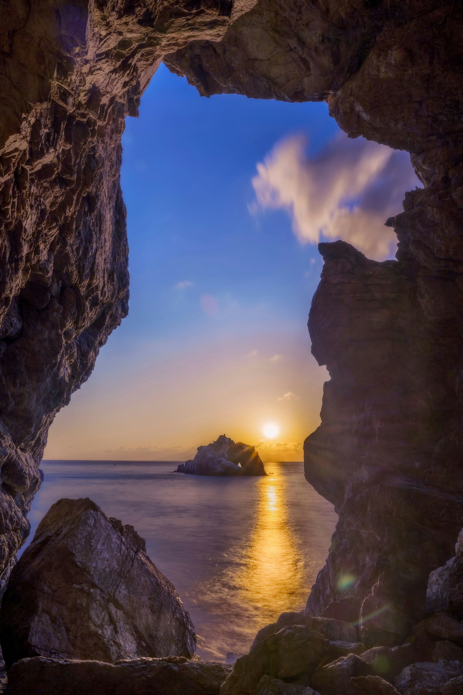 Blick auf den Sonnenuntergang über dem Meer, eingerahmt von einem felsigen Höhleneingang