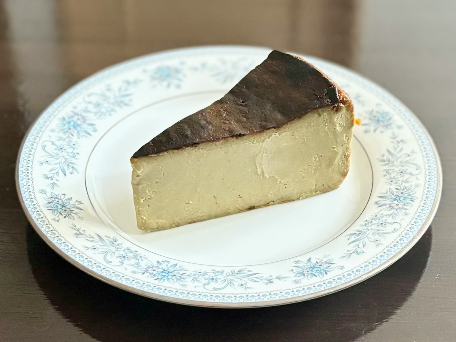 Una rebanada de queso cremoso con corteza negra en un plato con diseño floral azul