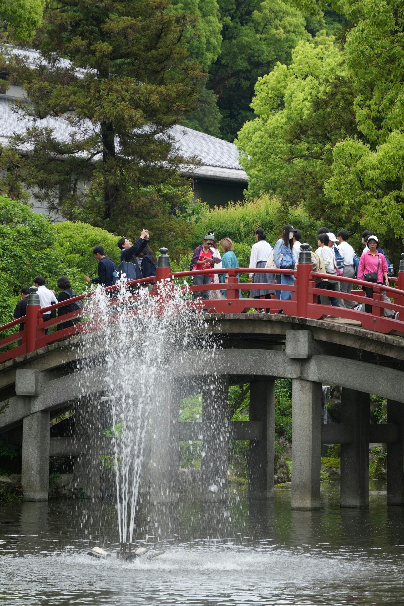 Touristen auf einer roten Brücke über einem Teich mit einem Brunnen