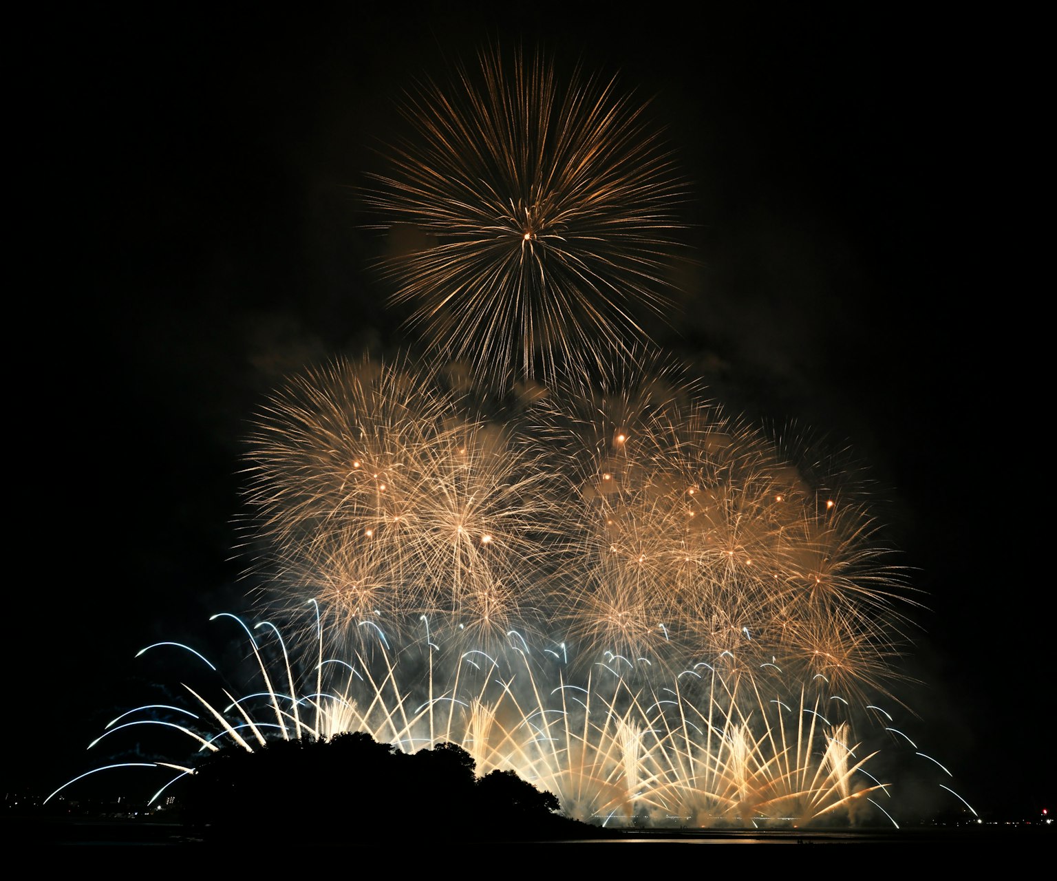 Fireworks display illuminating the night sky with bursts of golden light featuring a silhouetted island in the background