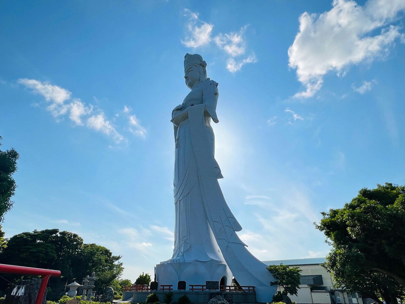 Eine riesige weiße Statue einer Gottheit steht unter einem blauen Himmel
