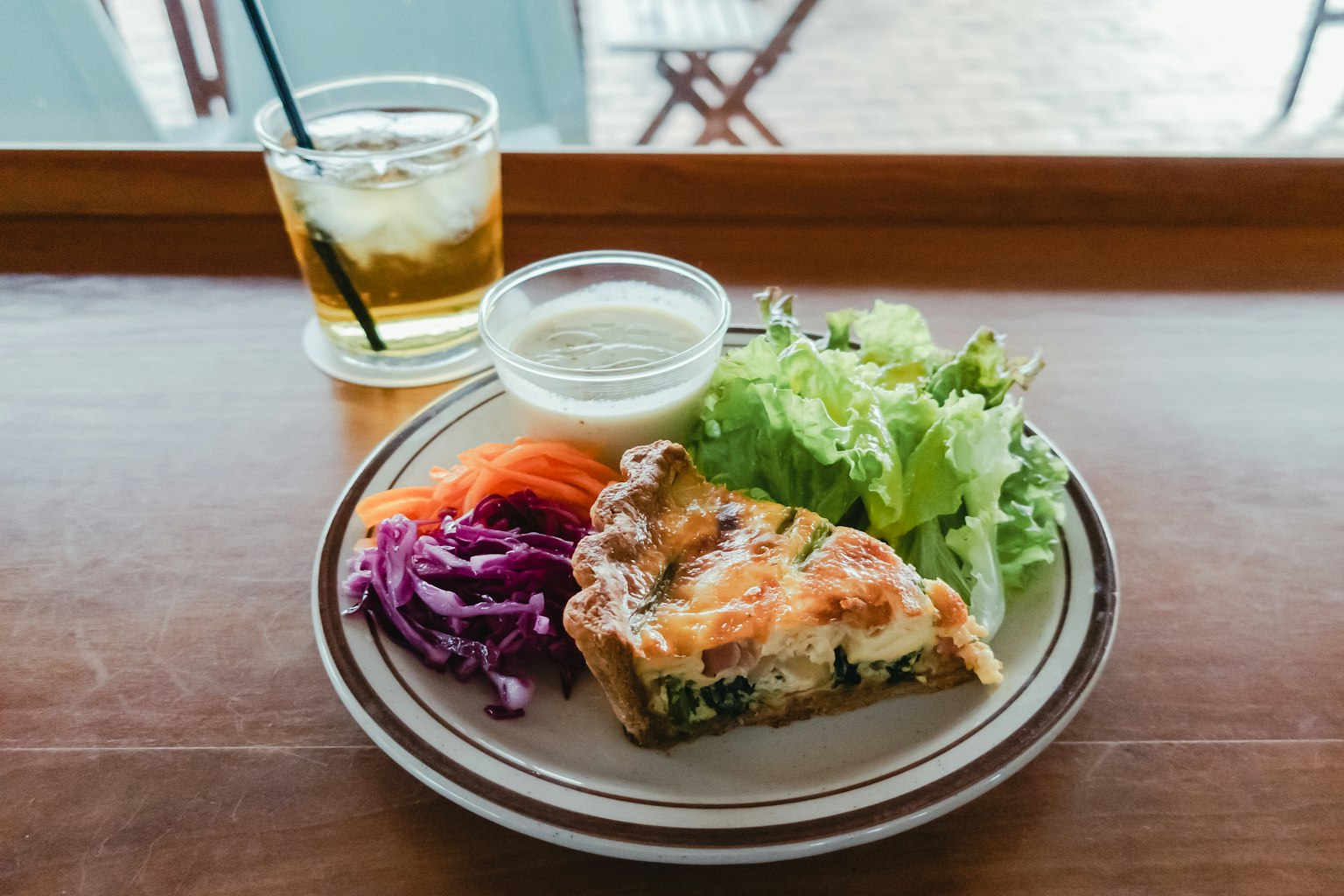 A plate with quiche salad and dipping sauce on a wooden table