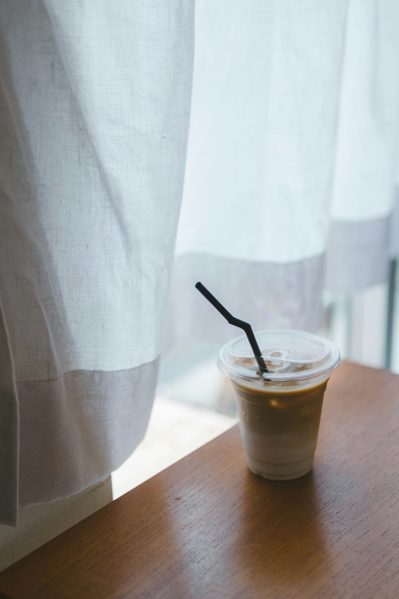 Tasse de café glacé à côté d'un rideau blanc