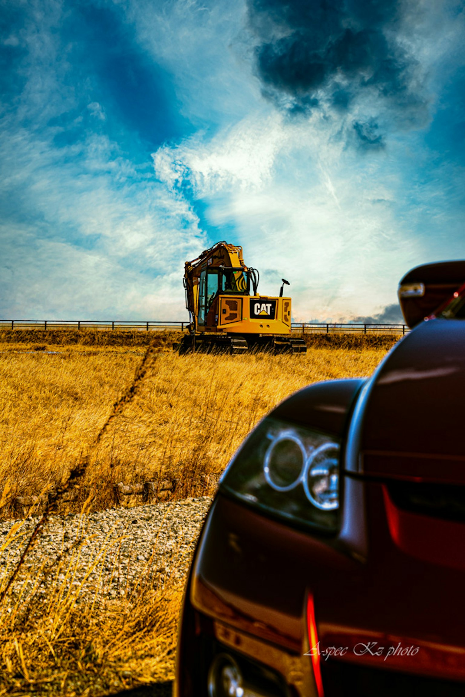 A red car with a close-up view and a yellow construction vehicle working in a vast field