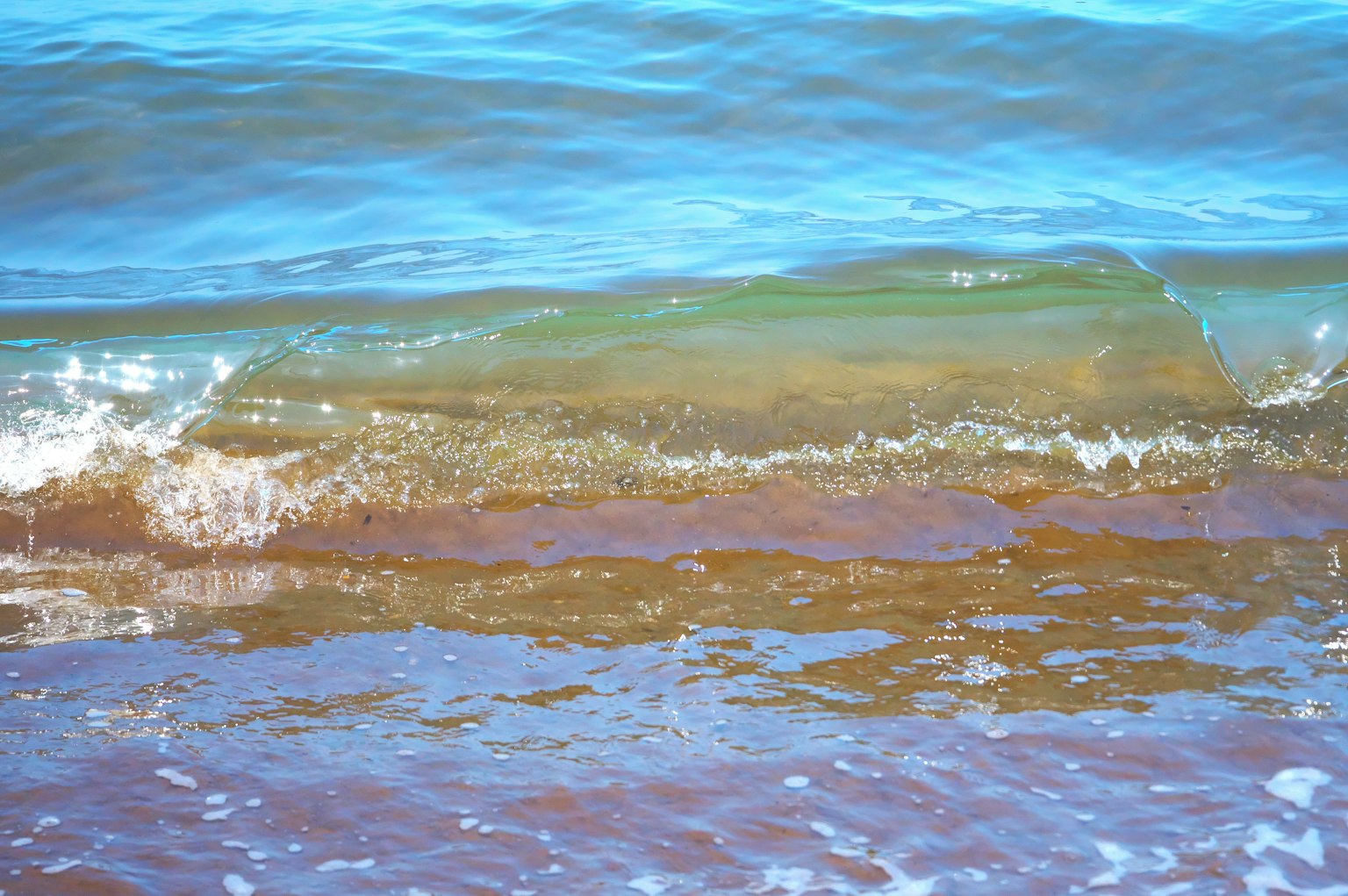 Wellen, die an den Strand rollen, mit einer blauen Wasseroberfläche und einem braunen Sandstrand