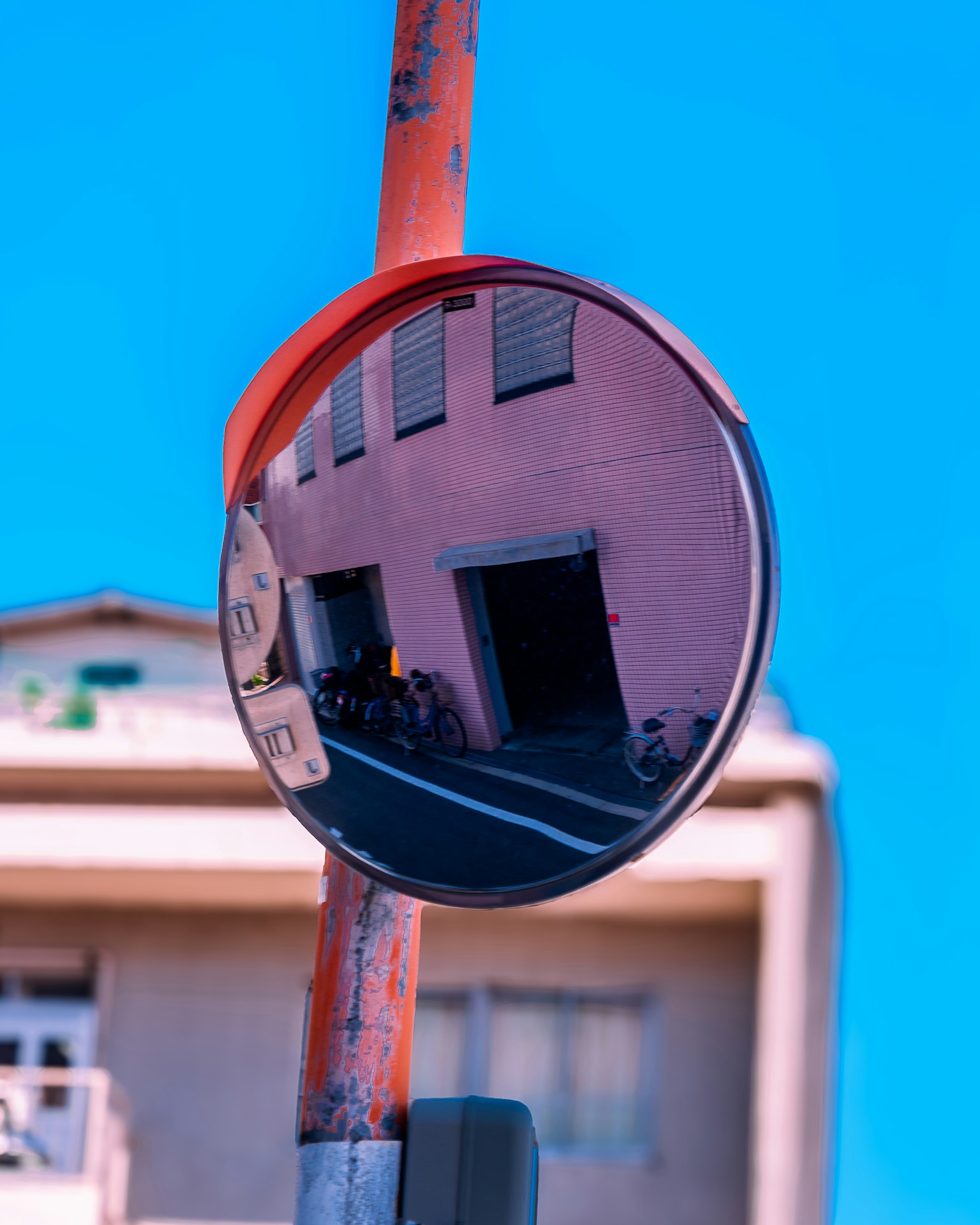 Reflektierender Straßenpiegel zeigt ein rosa Gebäude unter einem hellblauen Himmel
