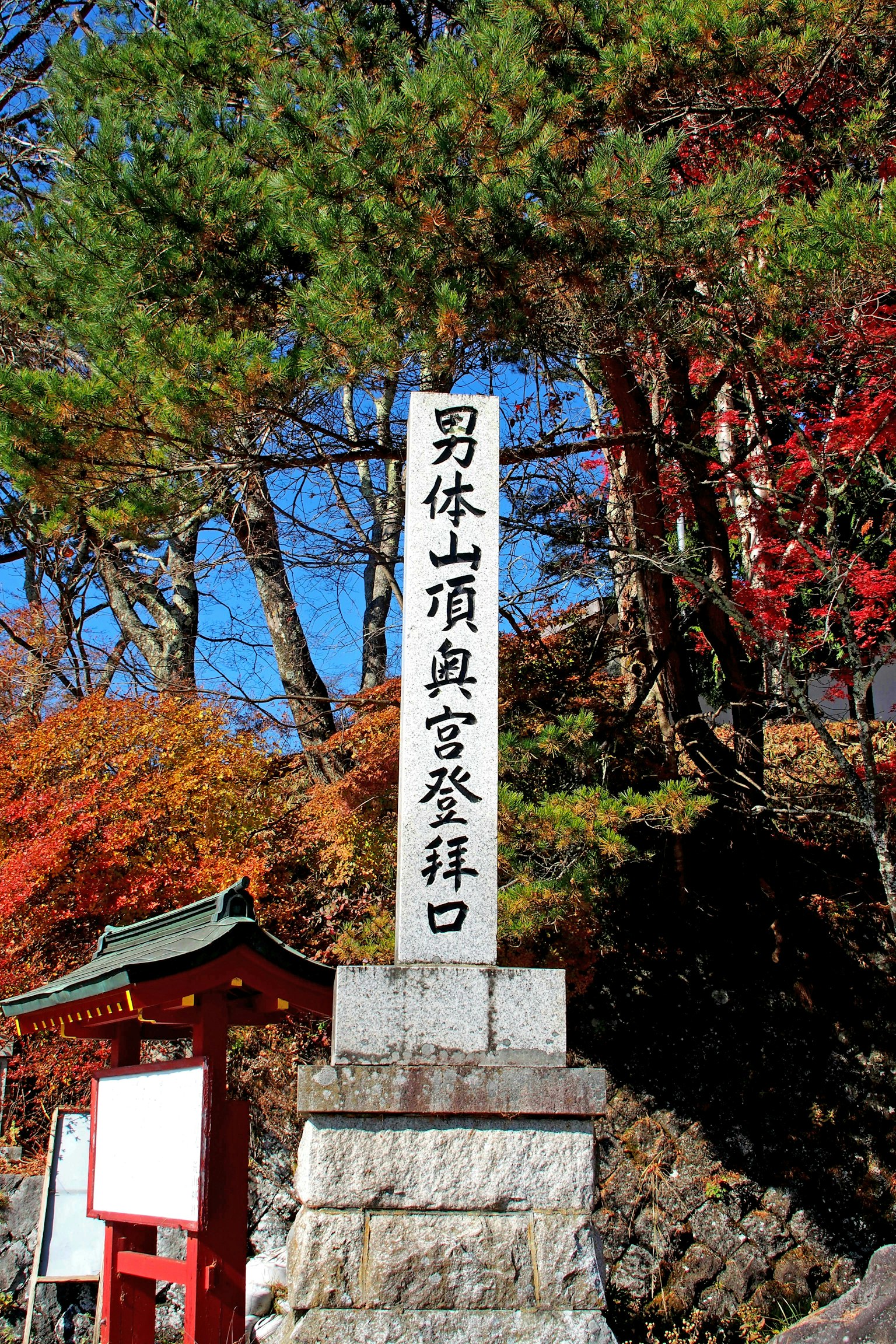 Stone monument marking the trailhead of Mount Nantai with autumn foliage