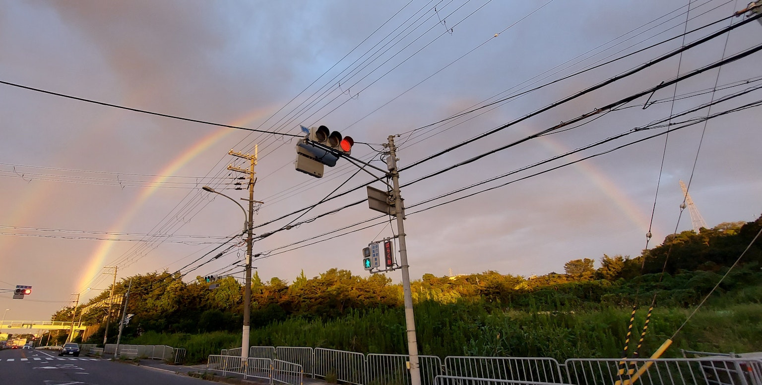 Vista di un arcobaleno sopra una strada con semafori e linee elettriche
