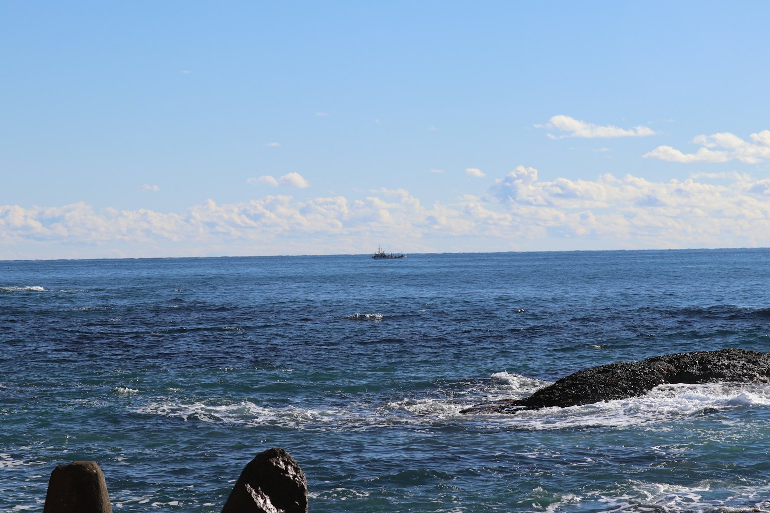 Océan bleu et ciel avec un bateau lointain et des rochers