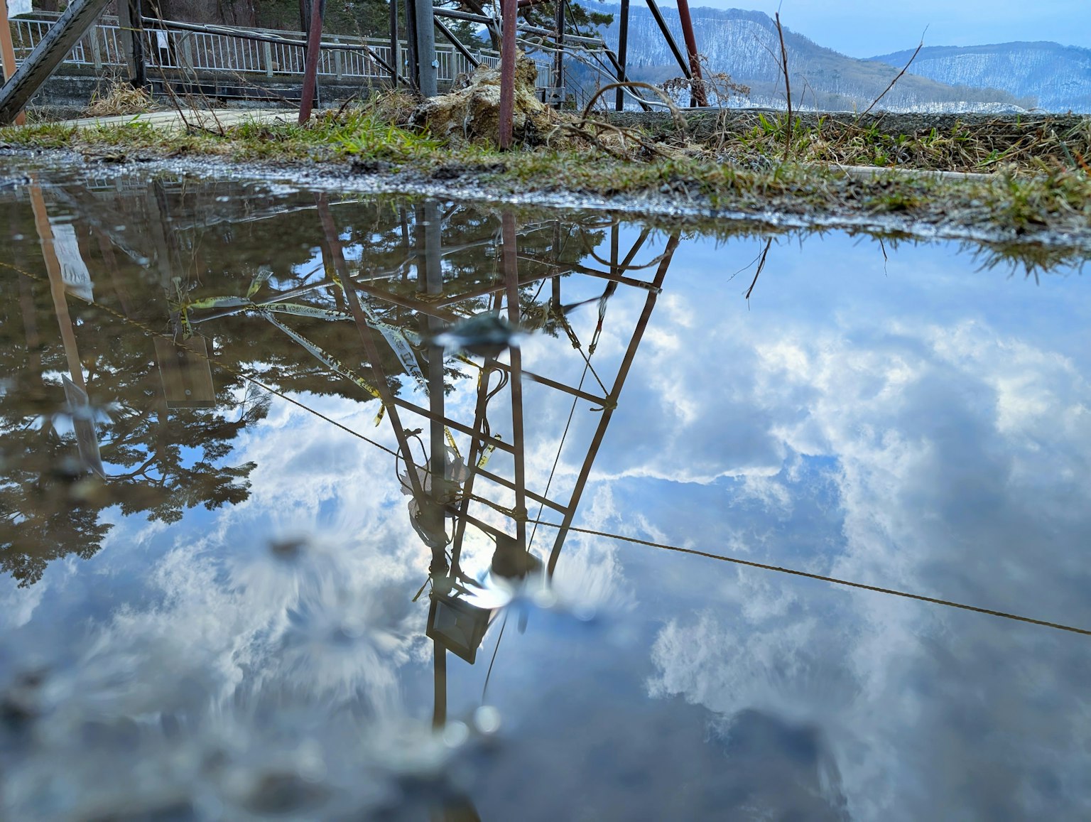 Réflexion du ciel bleu et des nuages dans une flaque structure métallique visible