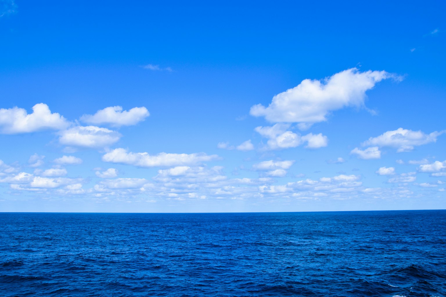 Vast blue ocean under a clear sky with white clouds
