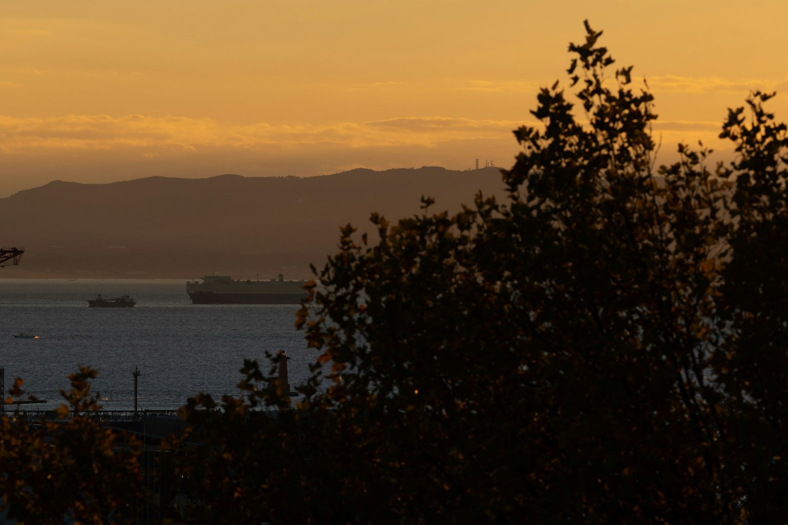 Silueta de barcos contra un atardecer sobre el mar y las montañas