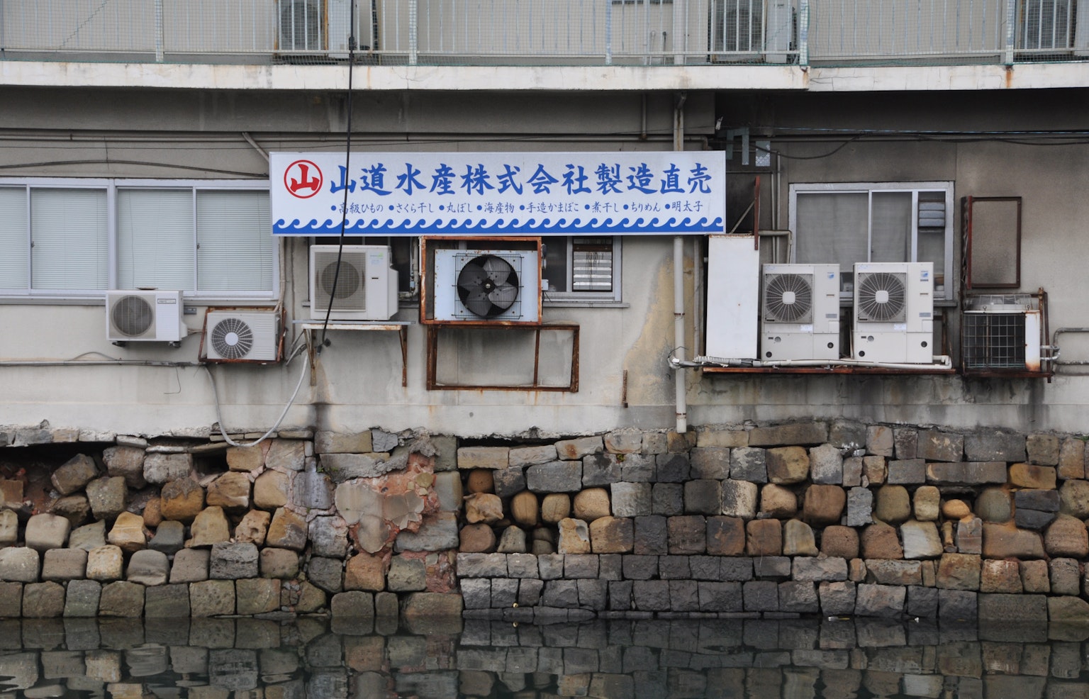 Pared de un edificio con unidades de aire acondicionado y un letrero cerca del agua