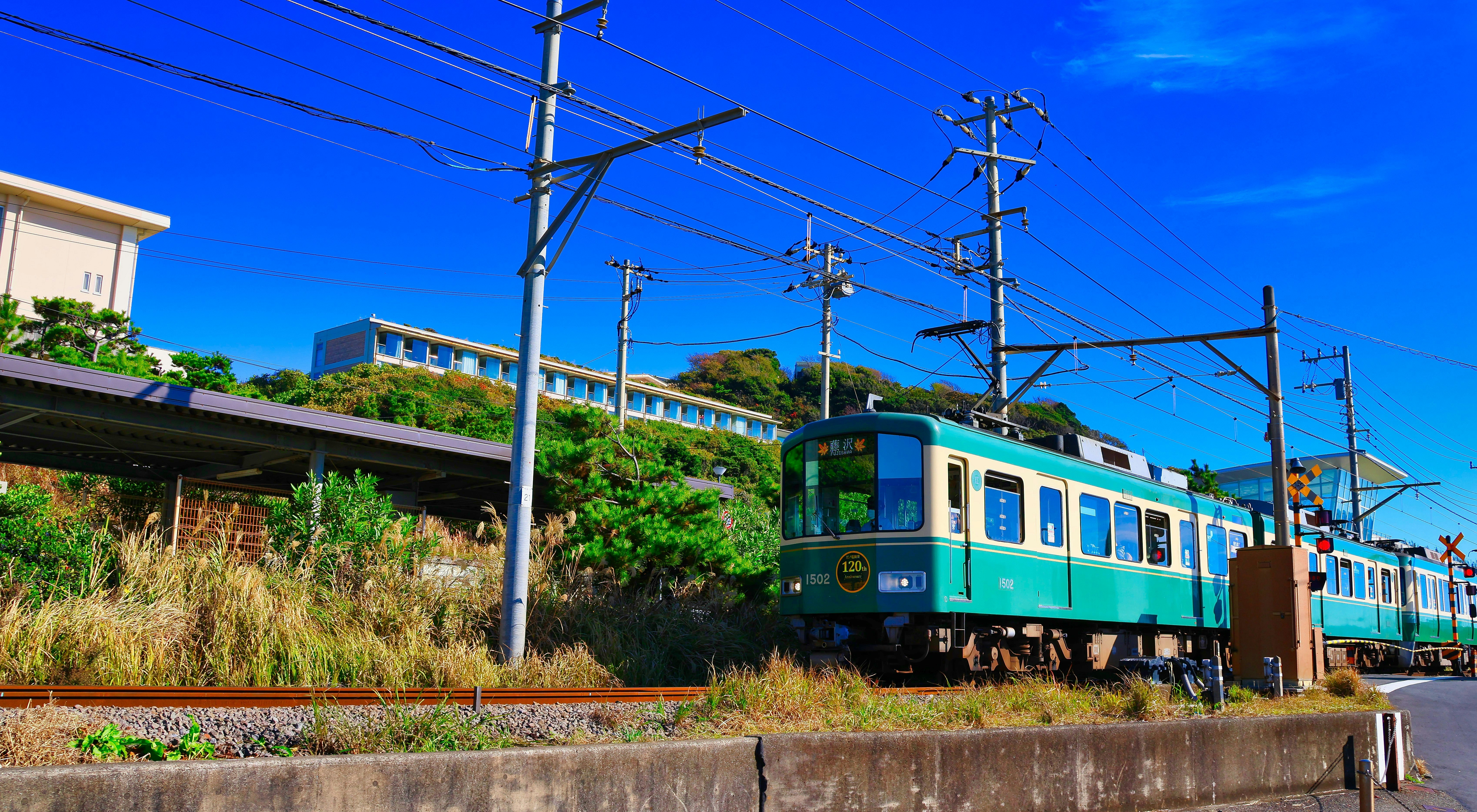 線路沿いを走る青緑の電車と架線のある風景