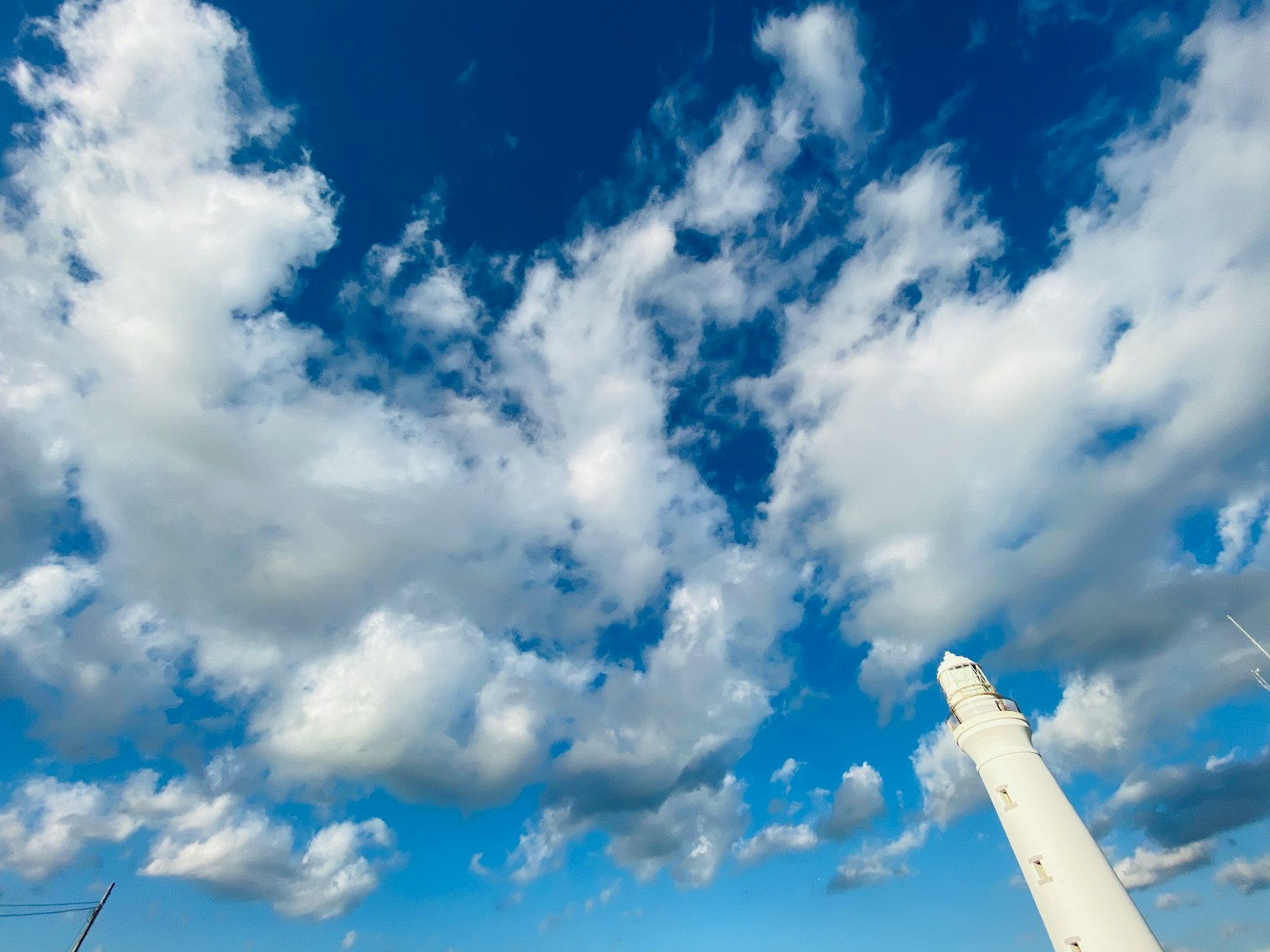 Cielo blu brillante pieno di nuvole bianche soffici e vista parziale di un faro