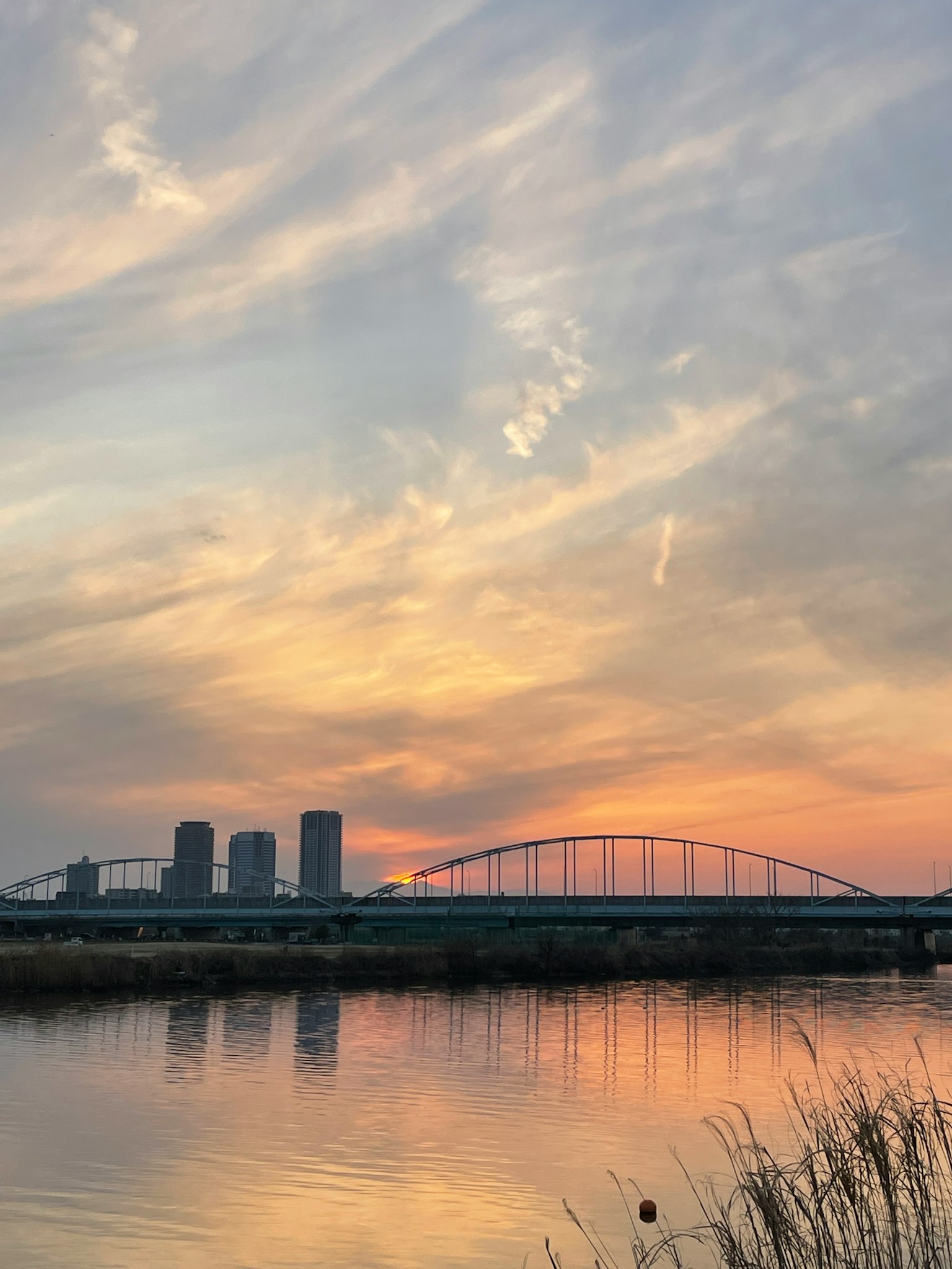 夕阳下的天空映射在水面上，有建筑和桥