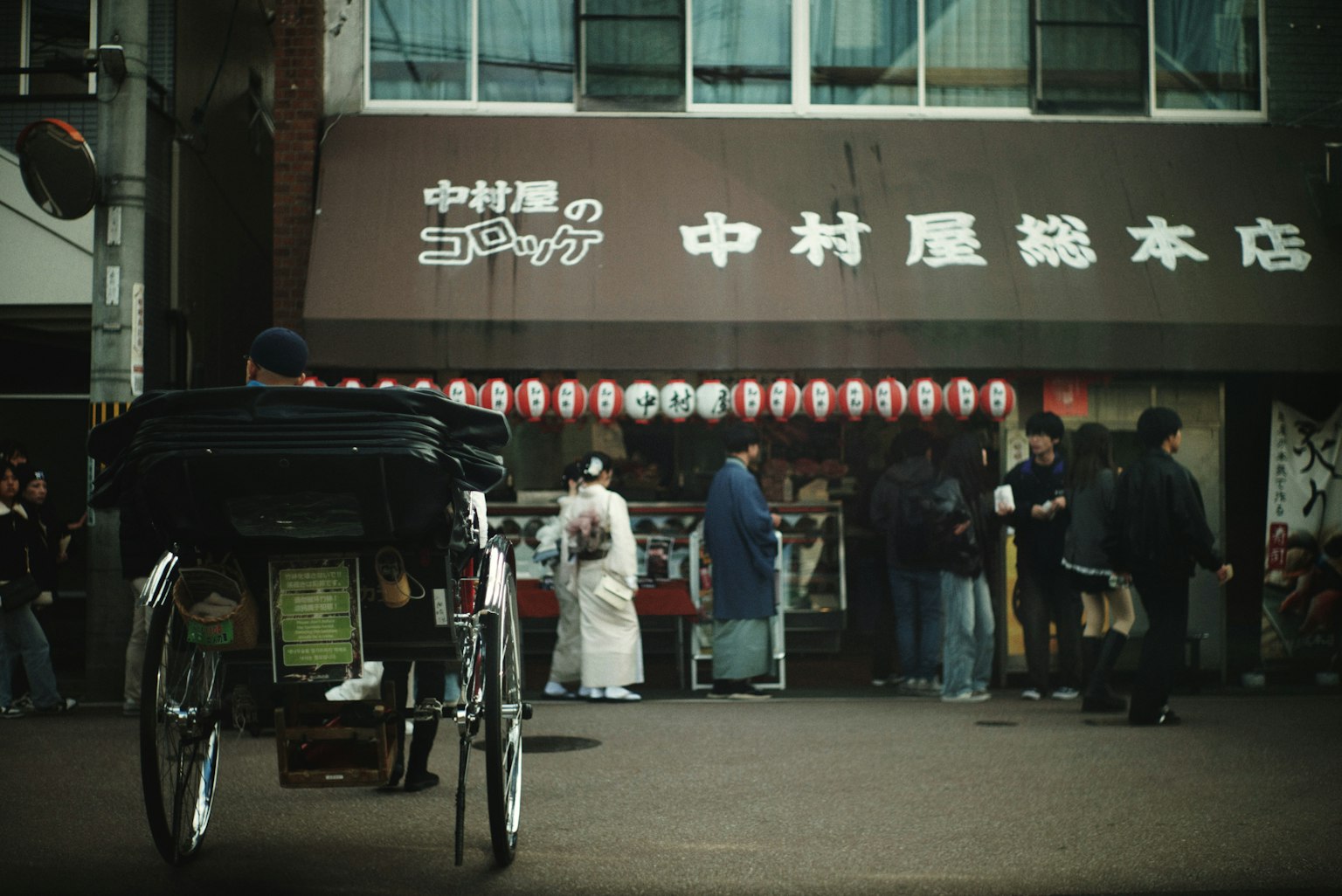 人力車が前景にあり、伝統的な和服を着た人々が店の前に並んでいる