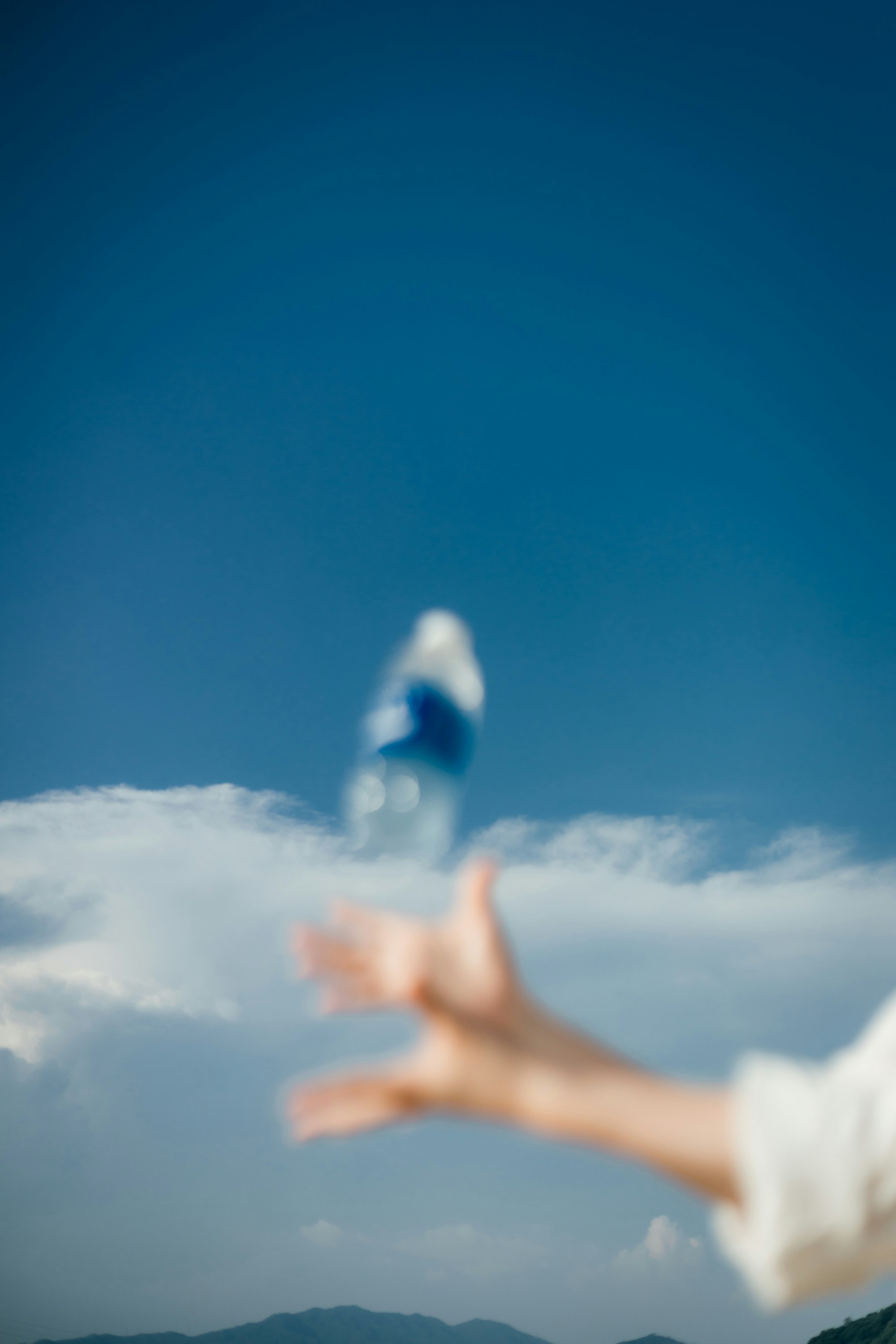 青空の下で雲と山を背景に飛ぶ人のシルエット