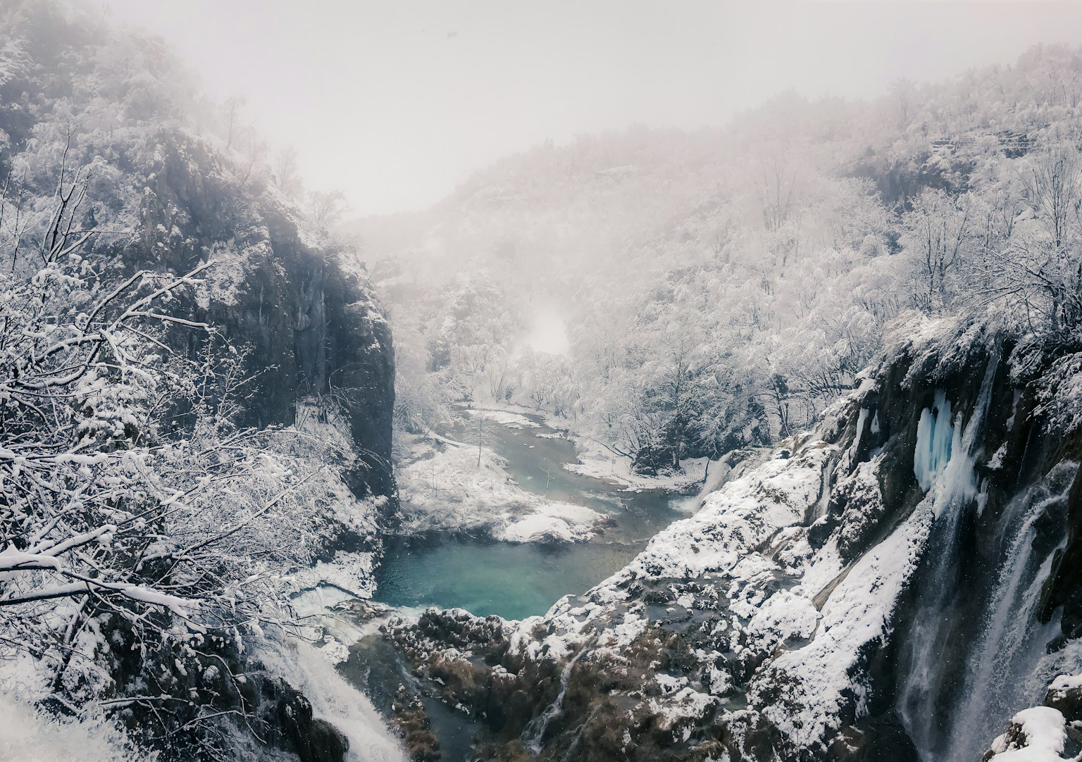 Vallée enneigée avec des cascades et une rivière bleue froide