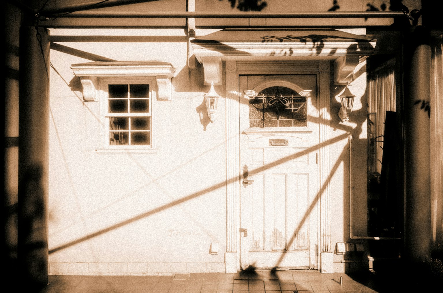 Exterior de una casa con pared blanca y puerta de madera Sombras dramáticas proyectadas por la luz del sol