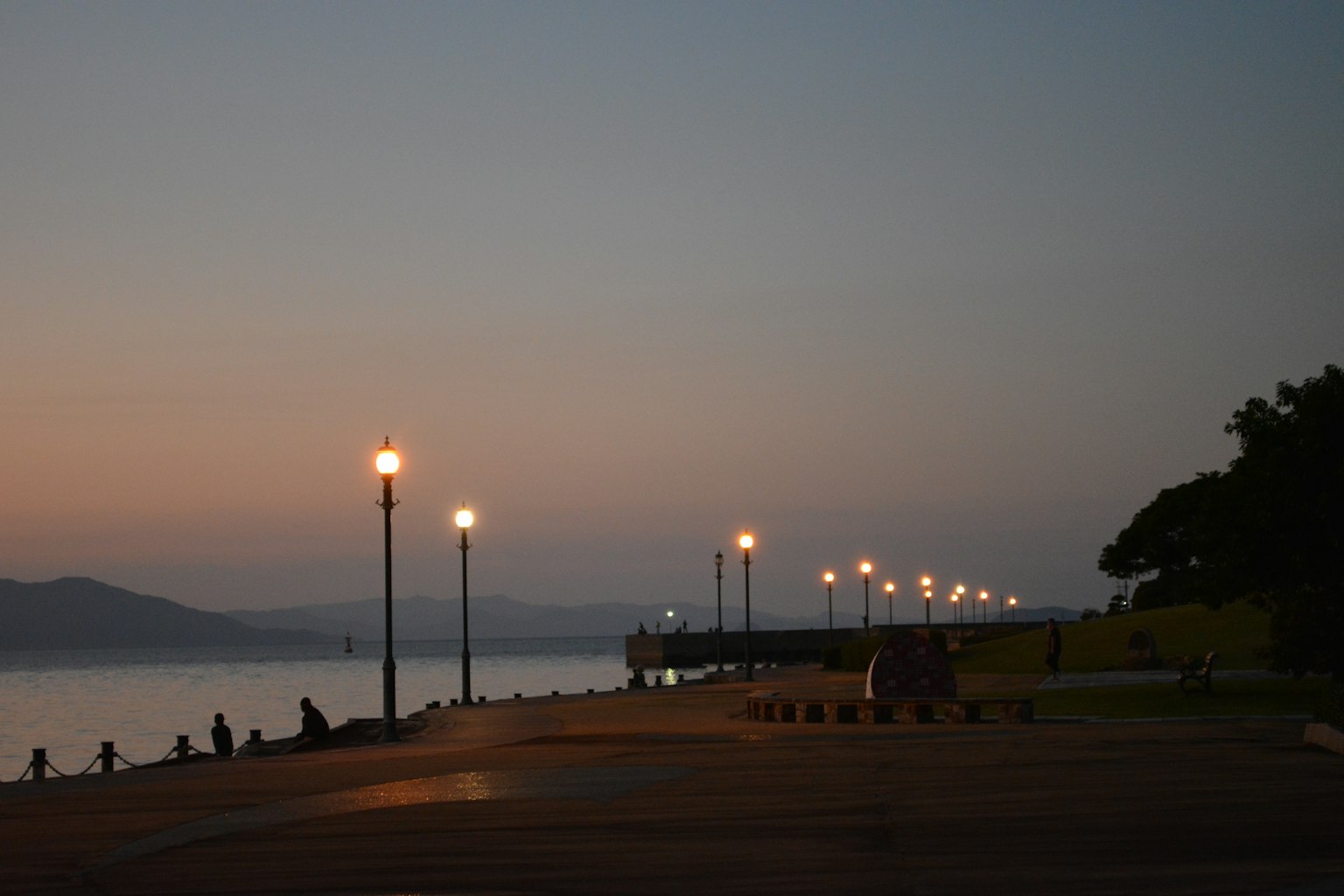 Paseo junto al agua al atardecer con farolas y personas