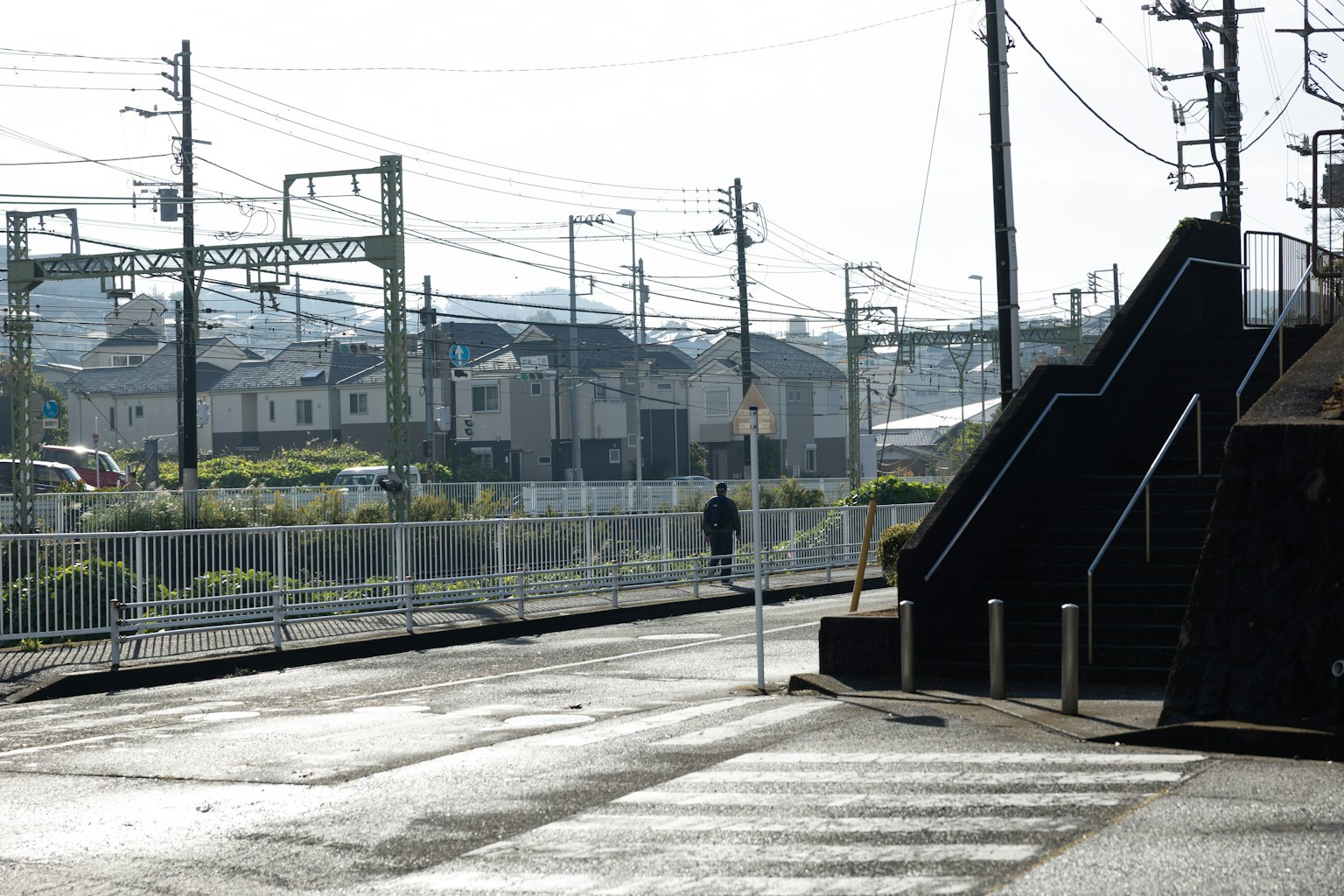 Eine ruhige städtische Szene mit einer einsamen Figur in der Nähe von Bahngleisen und Häusern im Hintergrund