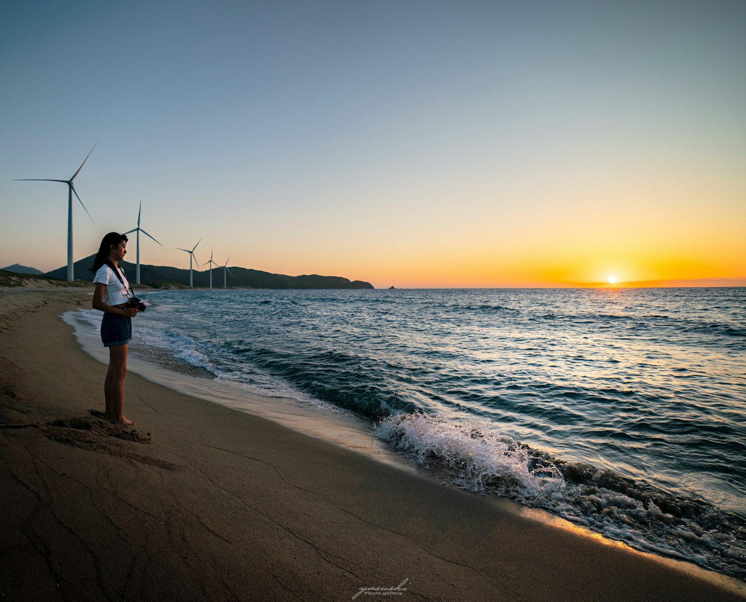 해변에서 일몰을 바라보는 여성 배경에 풍력 터빈이 있는