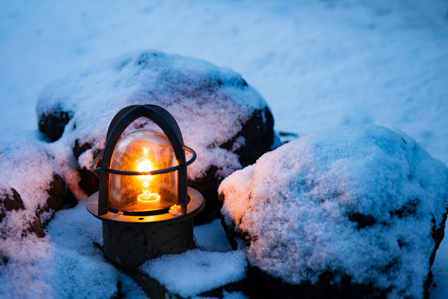 A lantern glowing warmly beside snow-covered rocks
