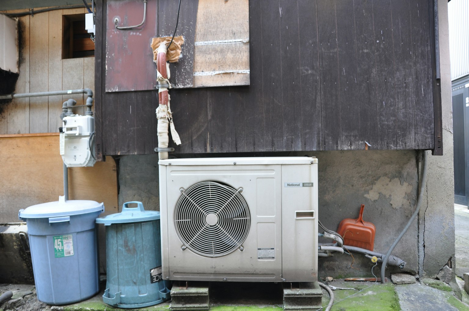Foto di un'unità di climatizzazione e bidoni della spazzatura dietro un vecchio edificio