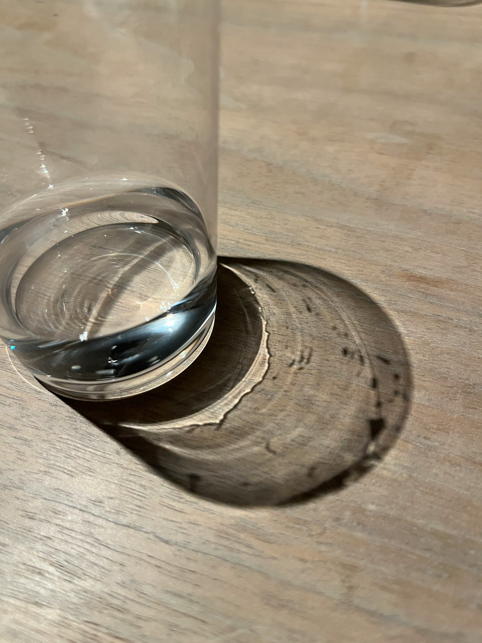 Bicchiere trasparente con acqua che proietta un'ombra su un tavolo di legno