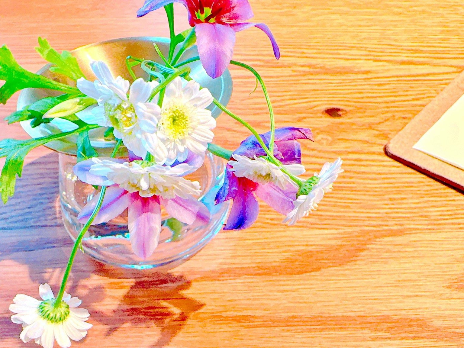 Eine klare Vase mit bunten Blumen auf einem Holztisch