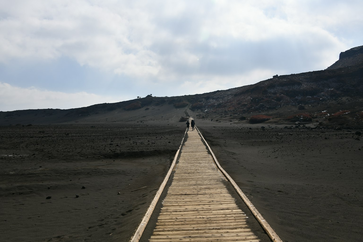 Holzweg, der sich durch eine öde Landschaft erstreckt, mit Menschen, die gehen