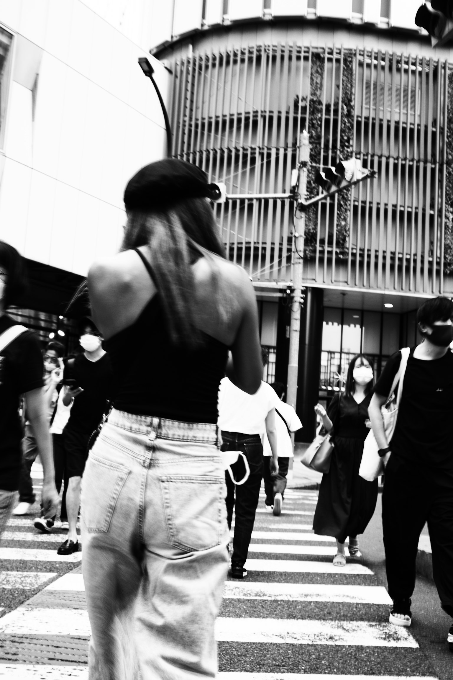 Seorang wanita berpakaian atasan hitam dan celana putih berjalan di zebra cross di lingkungan perkotaan