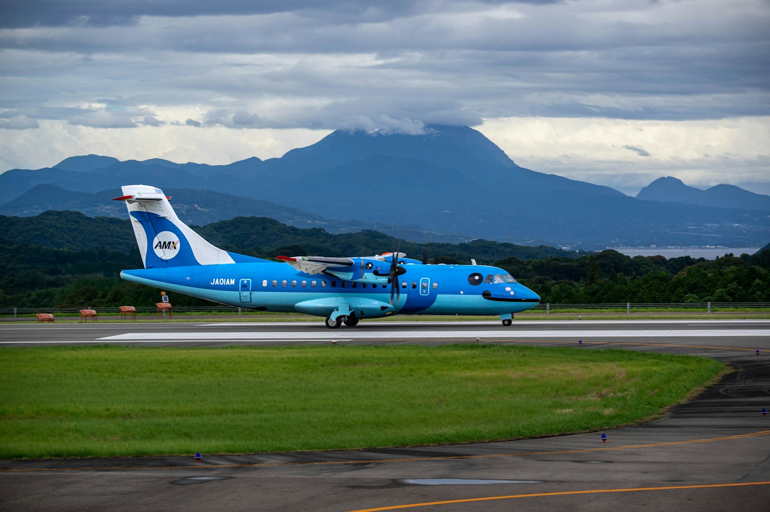 Ein blaues Flugzeug, das auf der Landebahn rollt, mit Bergen im Hintergrund