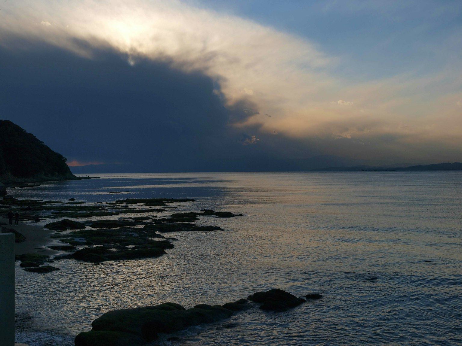 Coastal scene featuring rocks and calm water under dark clouds