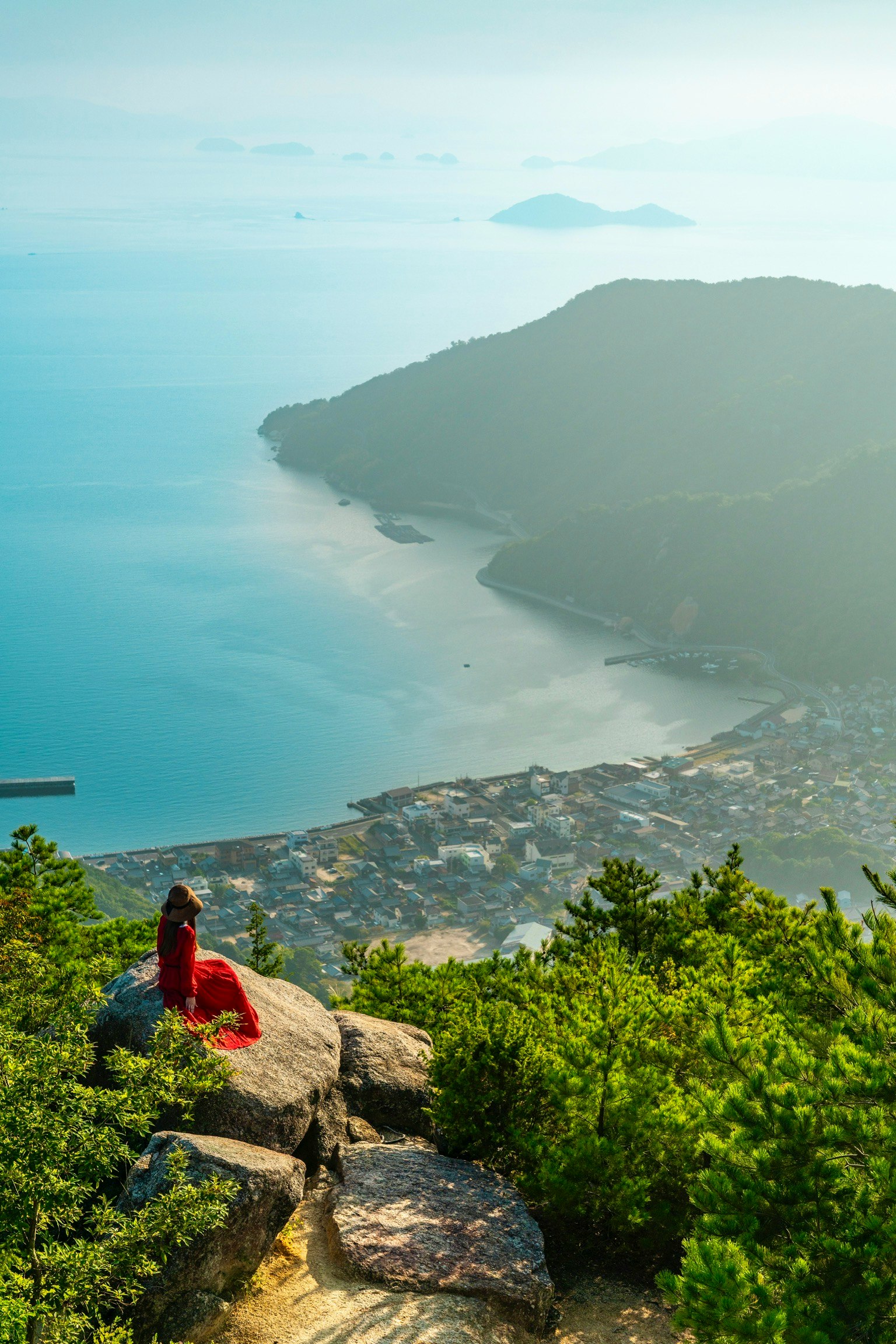 海と山の美しい景色を背景に赤い衣装を着た女性が座っている