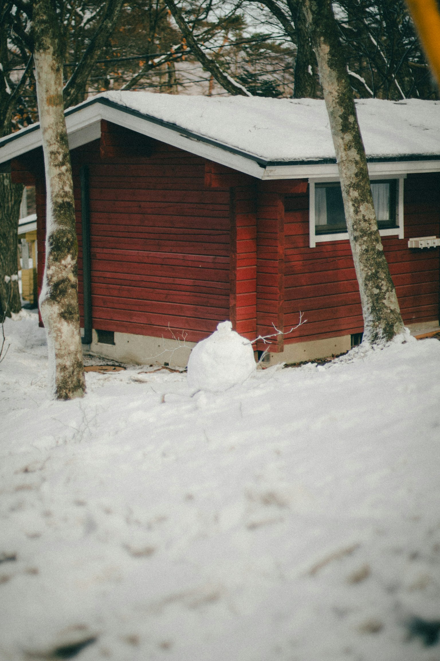 Scène d'hiver avec un cabanon rouge et un bonhomme de neige couvert de neige