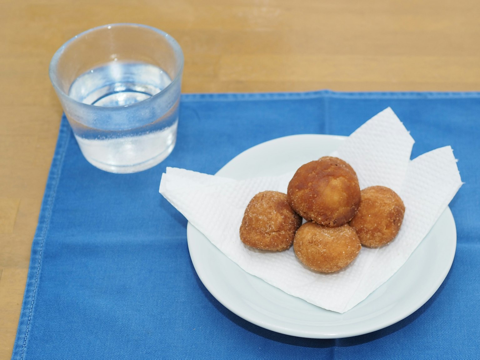 Palline fritte servite su un piatto bianco su una tovaglia blu con un bicchiere d'acqua
