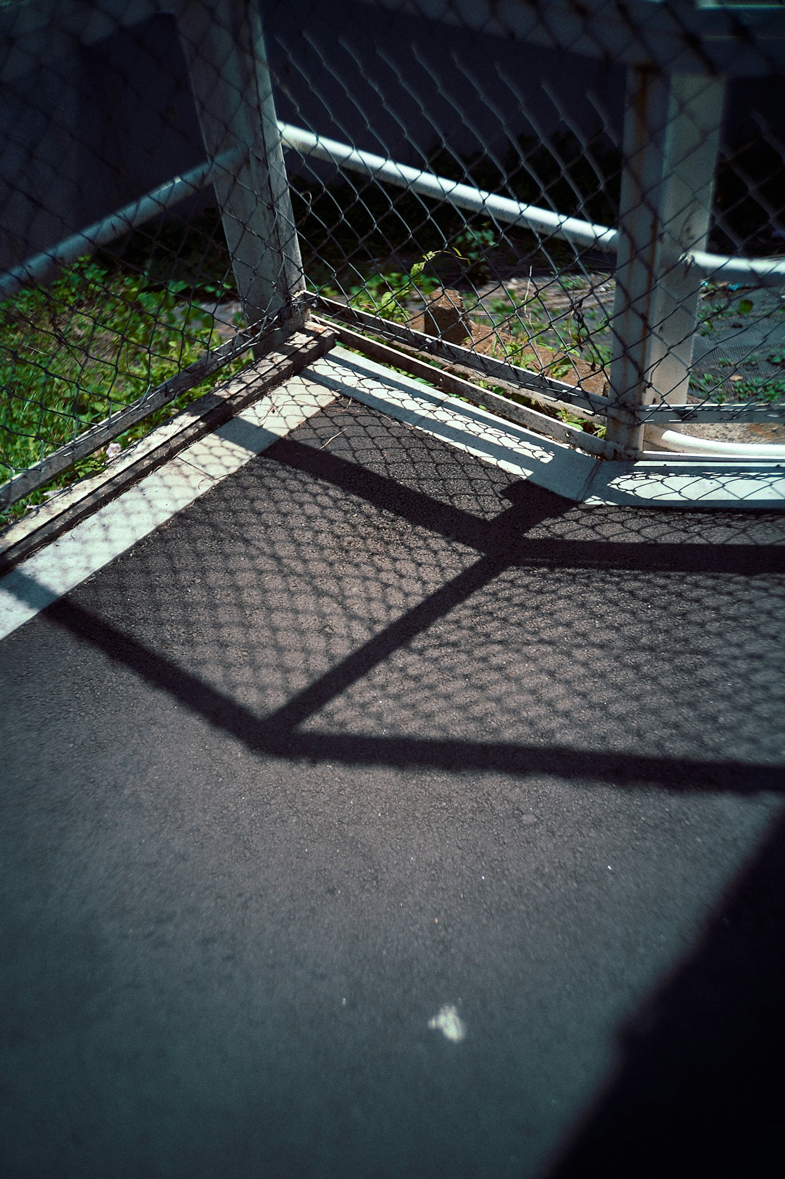 Bayangan pagar yang jatuh di tanah dengan rumput hijau yang terlihat