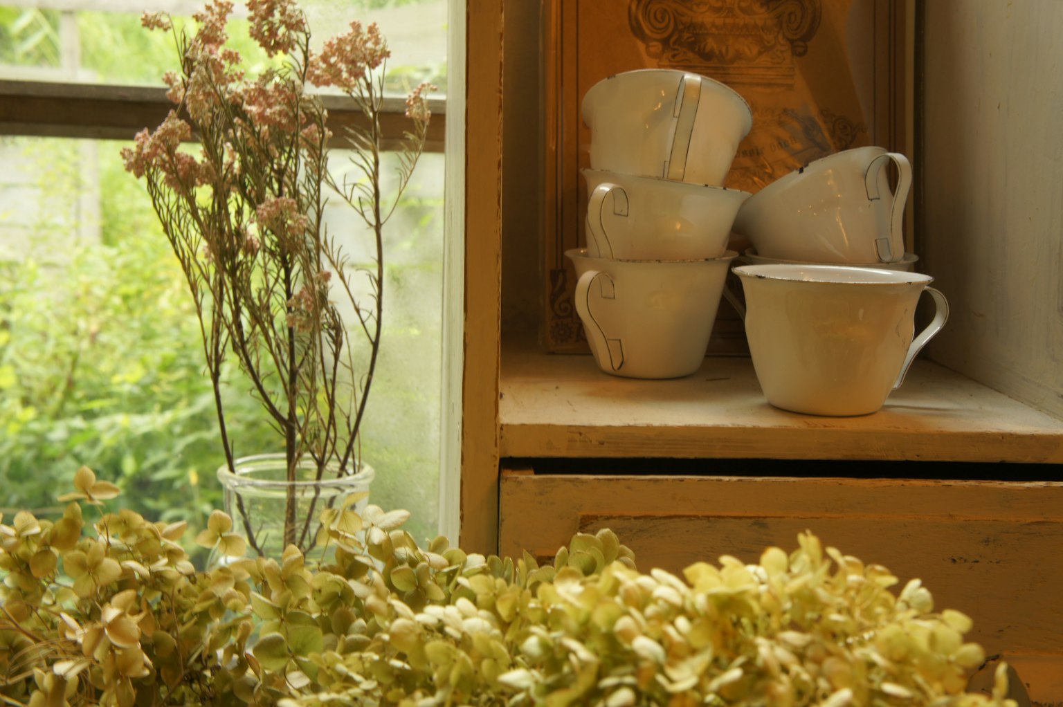 Stilleben mit getrockneten Blumen und Keramiktassen am Fenster