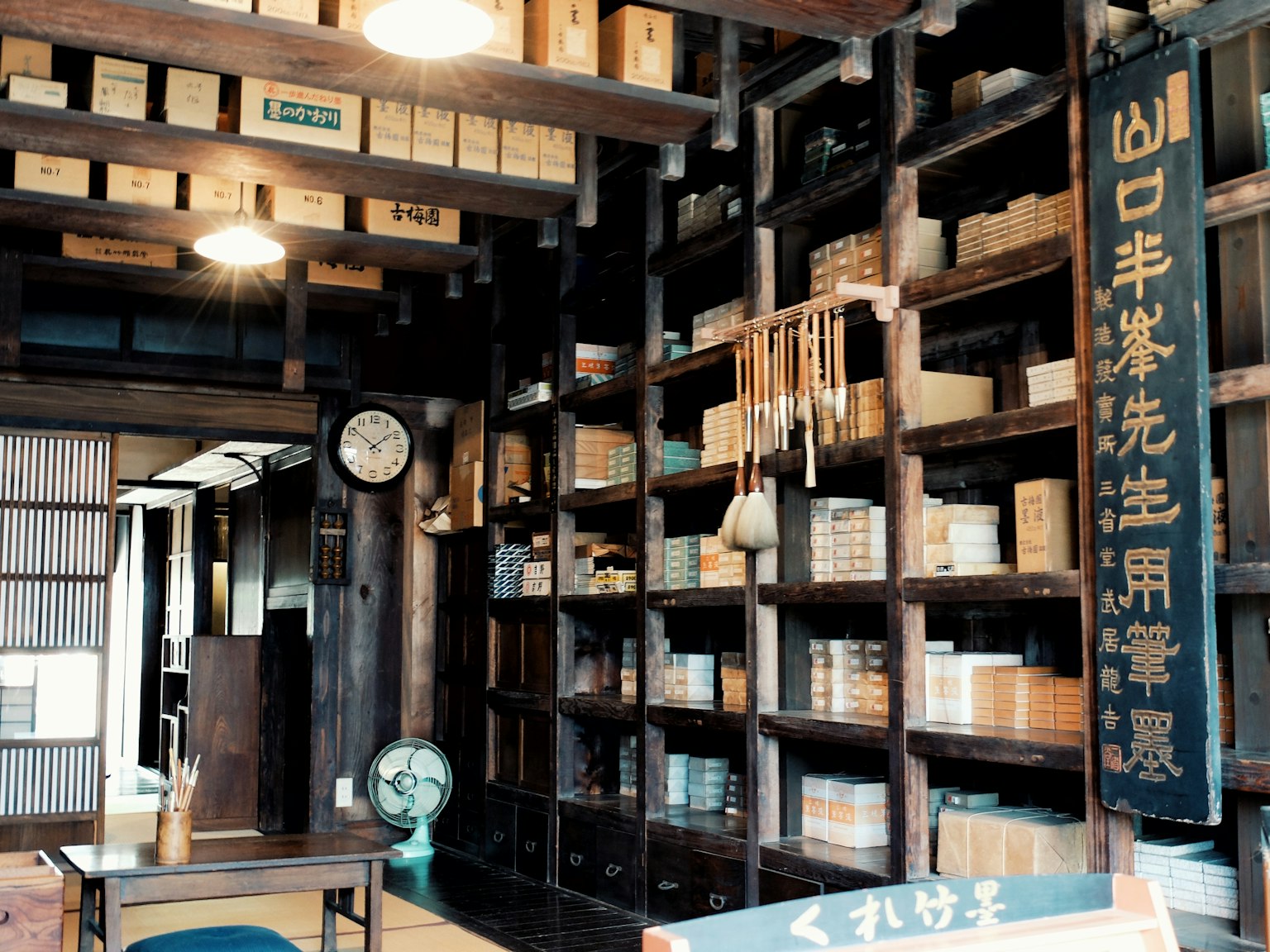 Traditionelles japanisches Ladeninterieur mit Holzregalen voll ordentlich angeordneter Kisten ein altes Schild an der Wand eine Uhr und ein Ventilator sichtbar