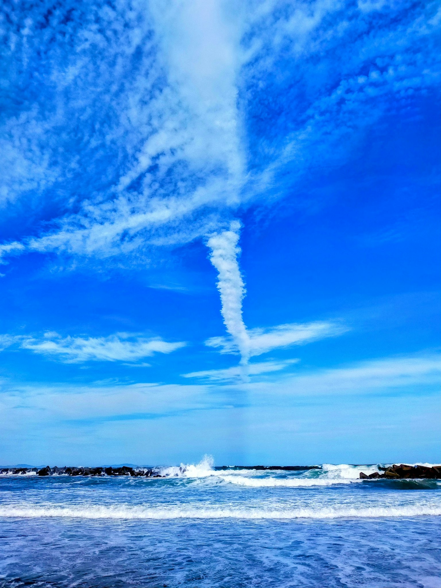 Una vista panoramica dell'oceano con onde e una formazione nuvolosa a spirale in un cielo blu