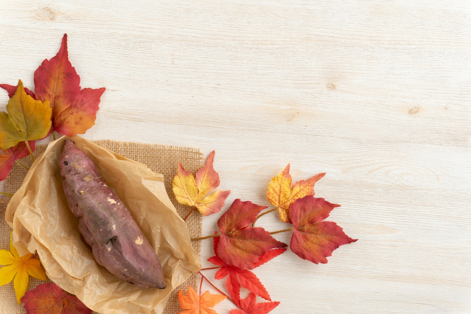 Sweet potato wrapped in paper surrounded by autumn leaves on a wooden table
