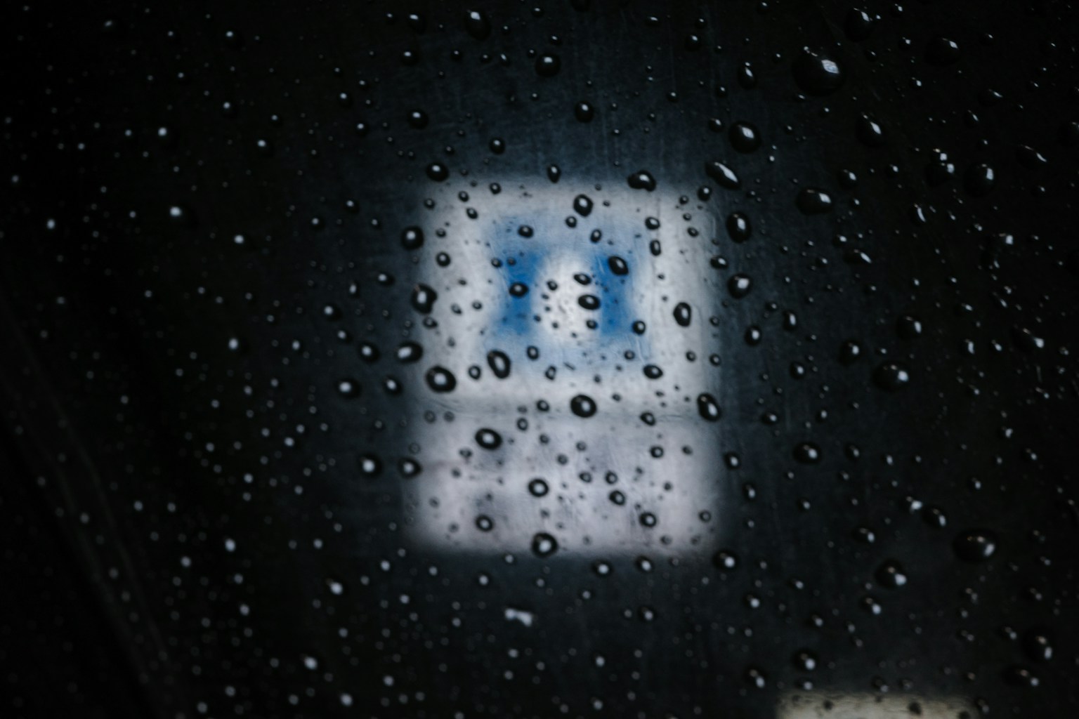 透過雨水斑點窗戶看到的模糊藍色標誌的圖像