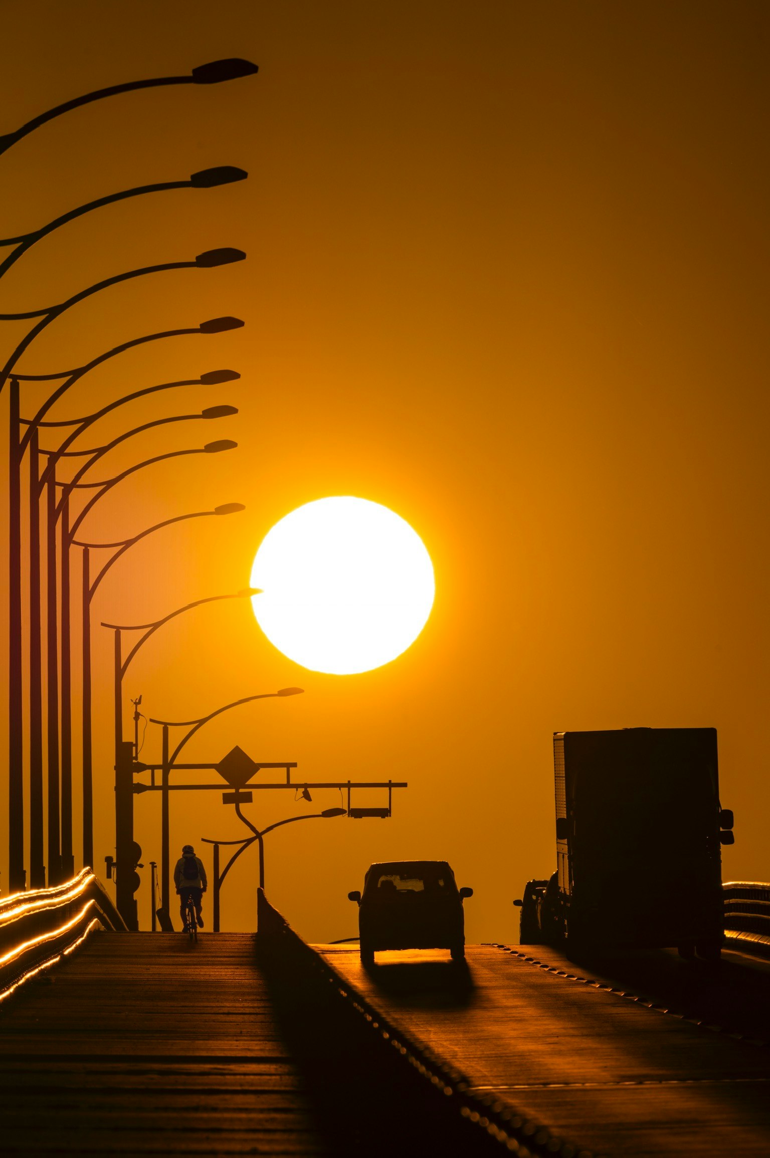 Silhouette du coucher de soleil sur un pont avec une voiture et une personne traversant