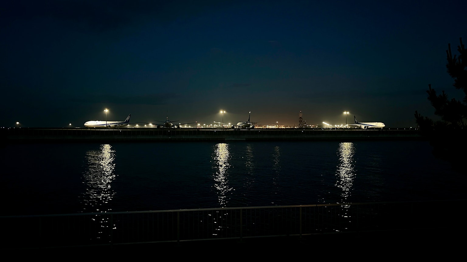 Vue nocturne d'un port avec des lumières se reflétant sur l'eau et des navires au loin