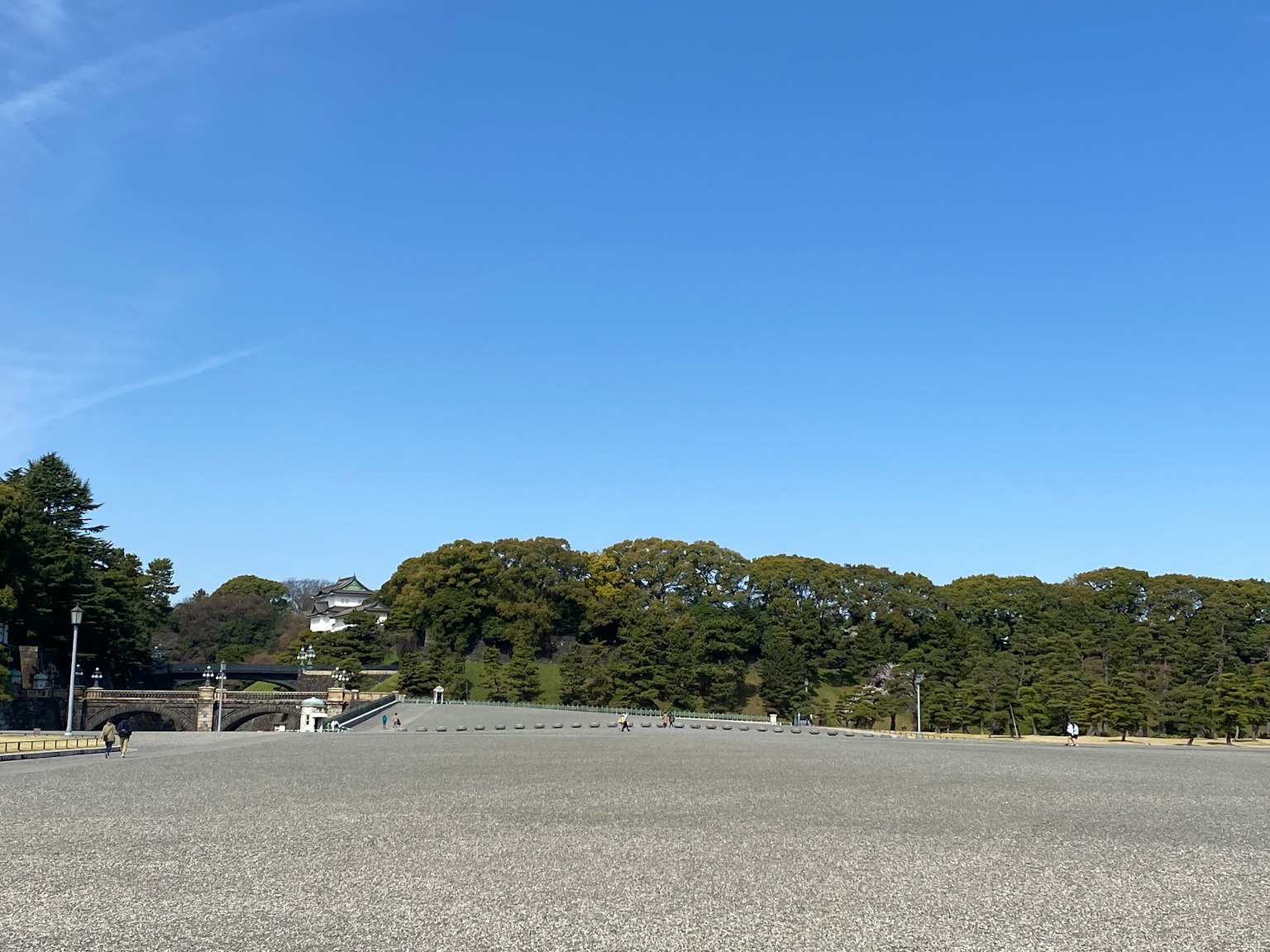 Wide gravel area under a clear blue sky with green trees