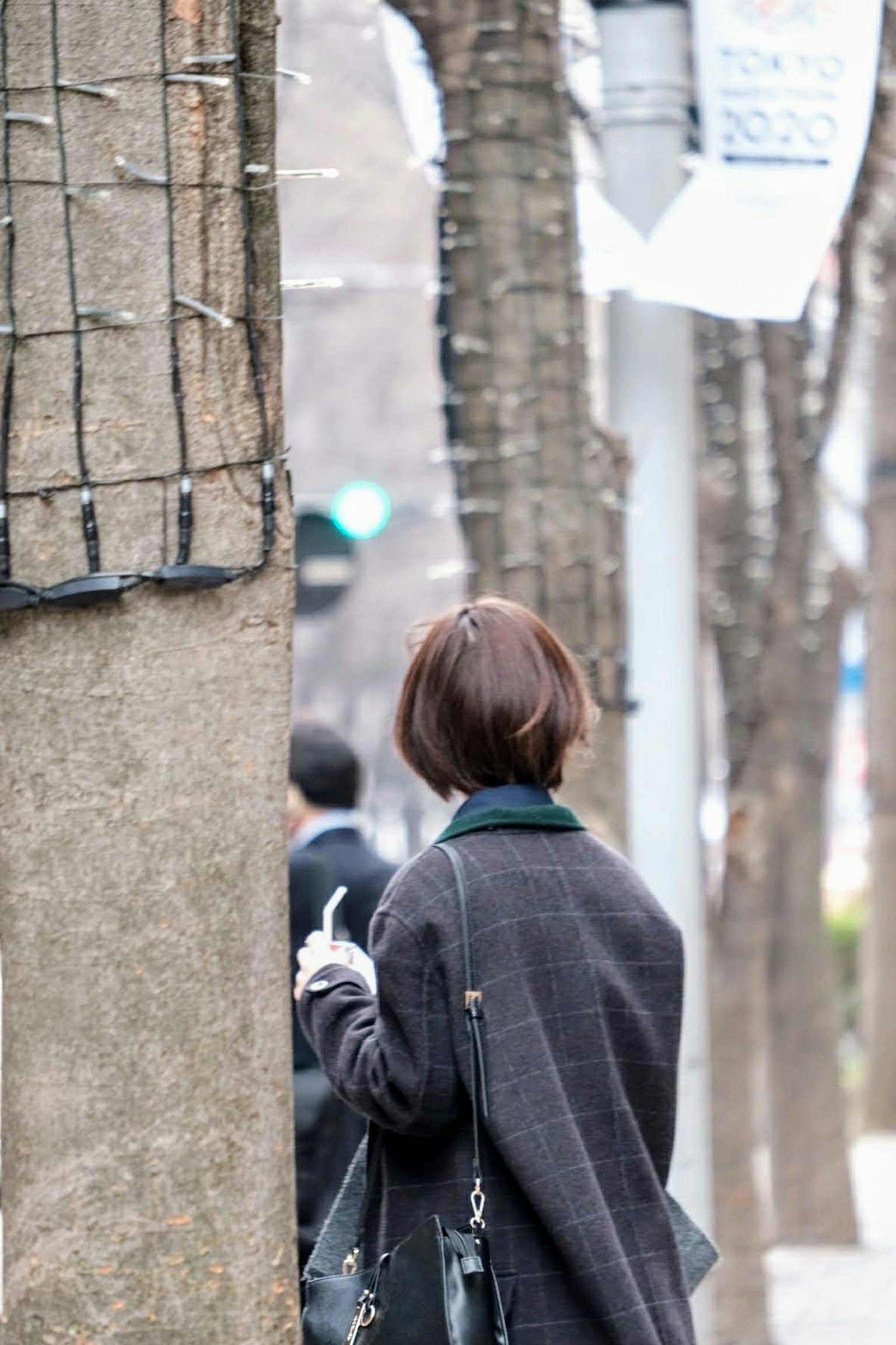 一名女性站在城市街道的一棵樹後面